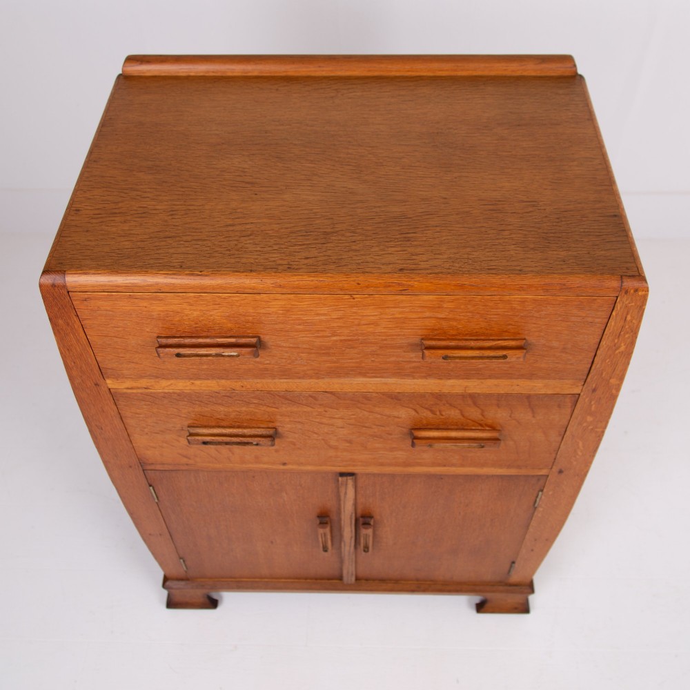 A 1930s Art Deco medium brown oak tallboy cabinet featuring two upper drawers with carved wooden handles and a double-door cupboard below. View VII
