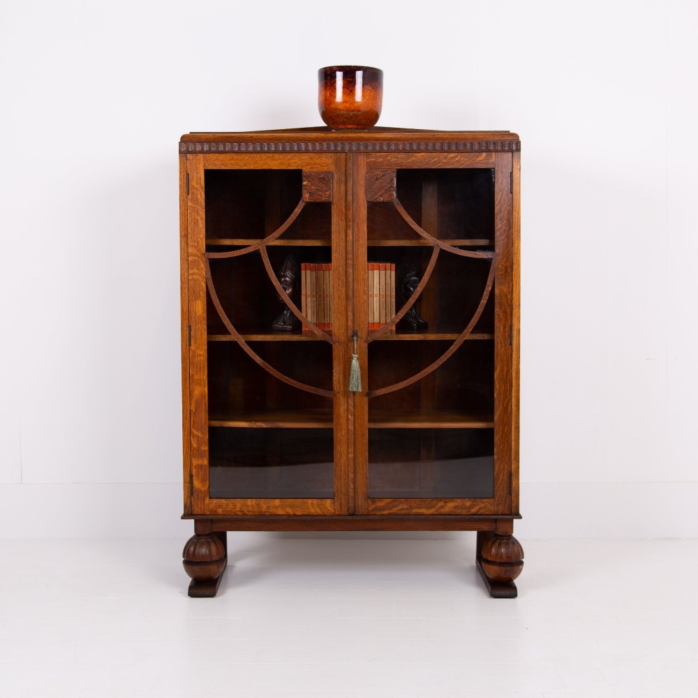 An Art Deco medium oak glazed bookcase featuring twin doors with decorative geometric wooden glazing bars and squat turned feet.