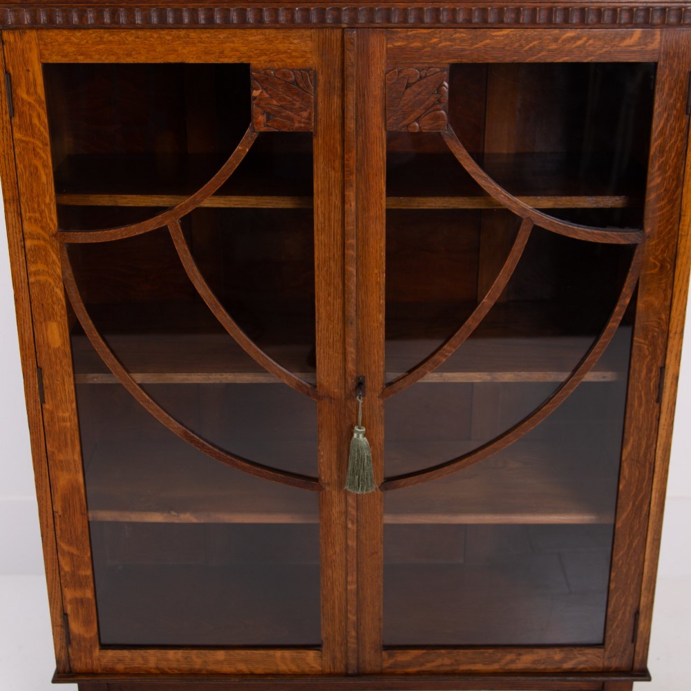 An Art Deco medium oak glazed bookcase featuring twin doors with decorative geometric wooden glazing bars and squat turned feet. View XI