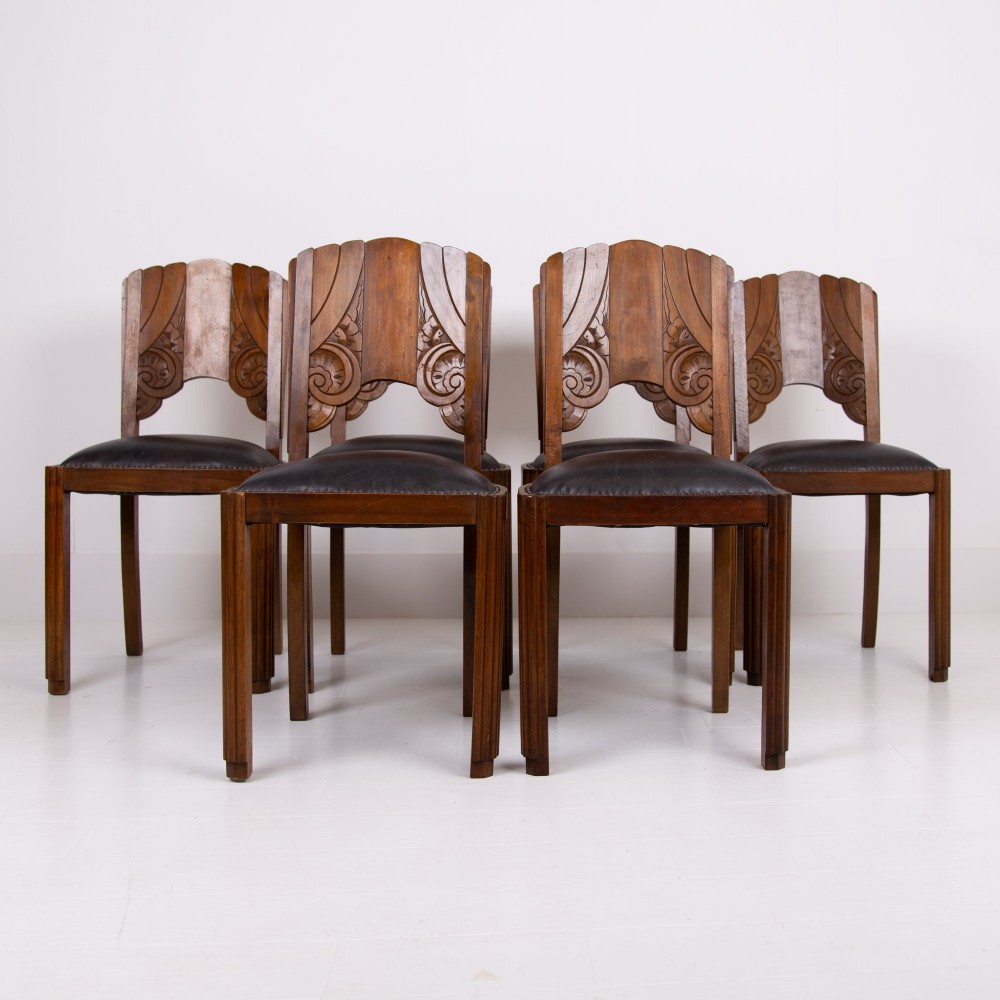 A set of four dark walnut dining chairs featuring carved sunburst motifs on the backs and dark leather upholstered seats.