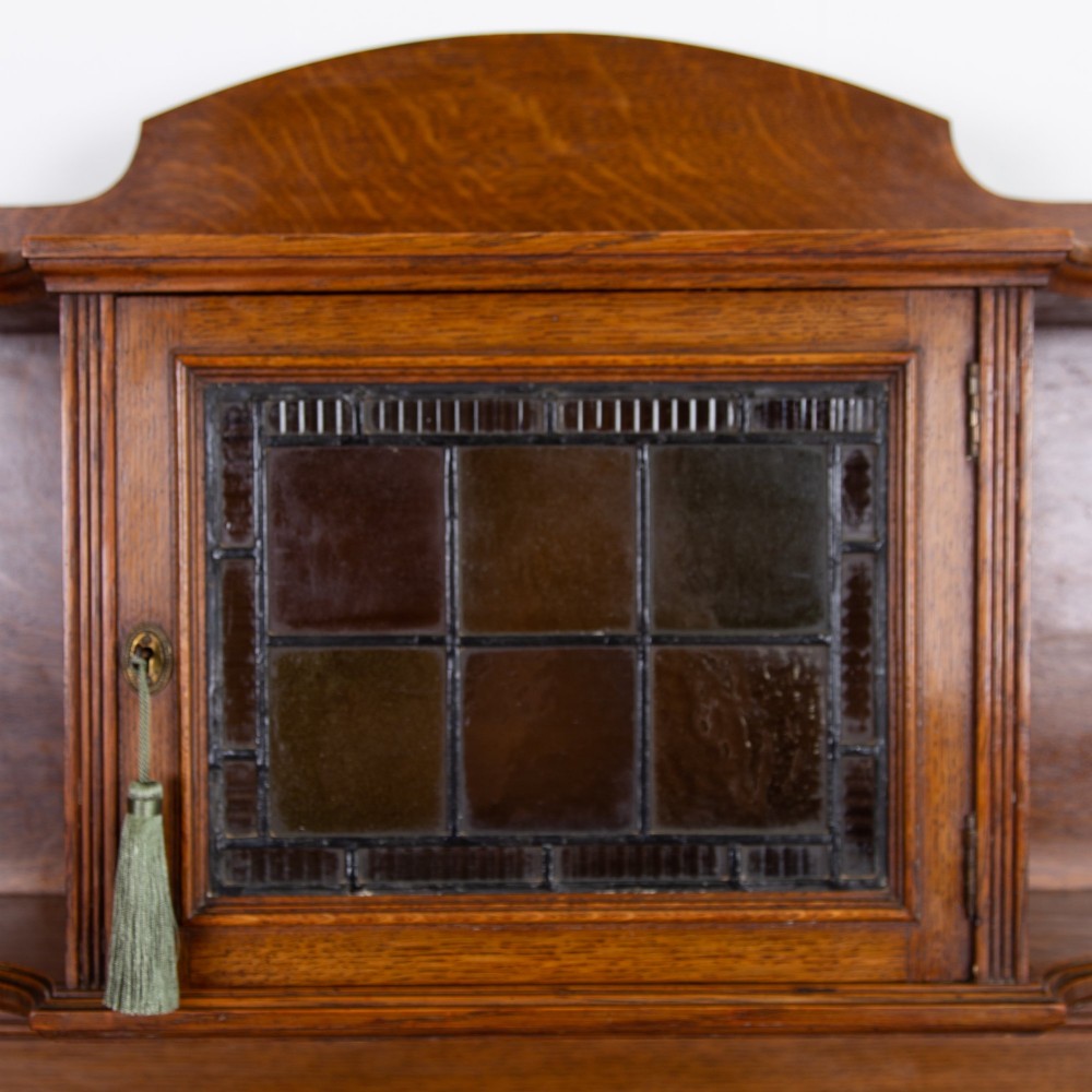 An Arts and Crafts oak cabinet dresser featuring an upper shelf unit with a central stained glass cabinet door, side heart cutouts, lower cupboards, a single drawer, and an open side niche. View IX
