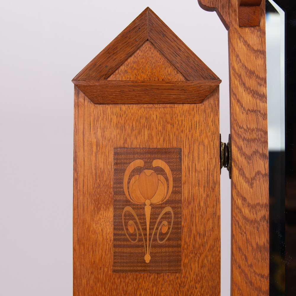 An Arts and Crafts oak dressing chest featuring a superstructure with a central mirror, inlaid side panels, and small jewellery drawers above a chest of drawers. View III
