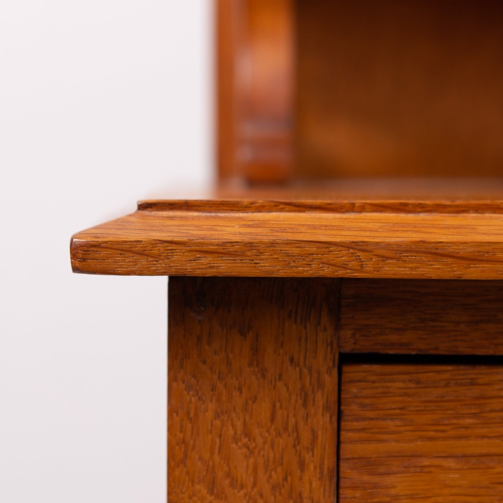 An Arts and Crafts oak dressing chest featuring a superstructure with a central mirror, inlaid side panels, and small jewellery drawers above a chest of drawers. View V