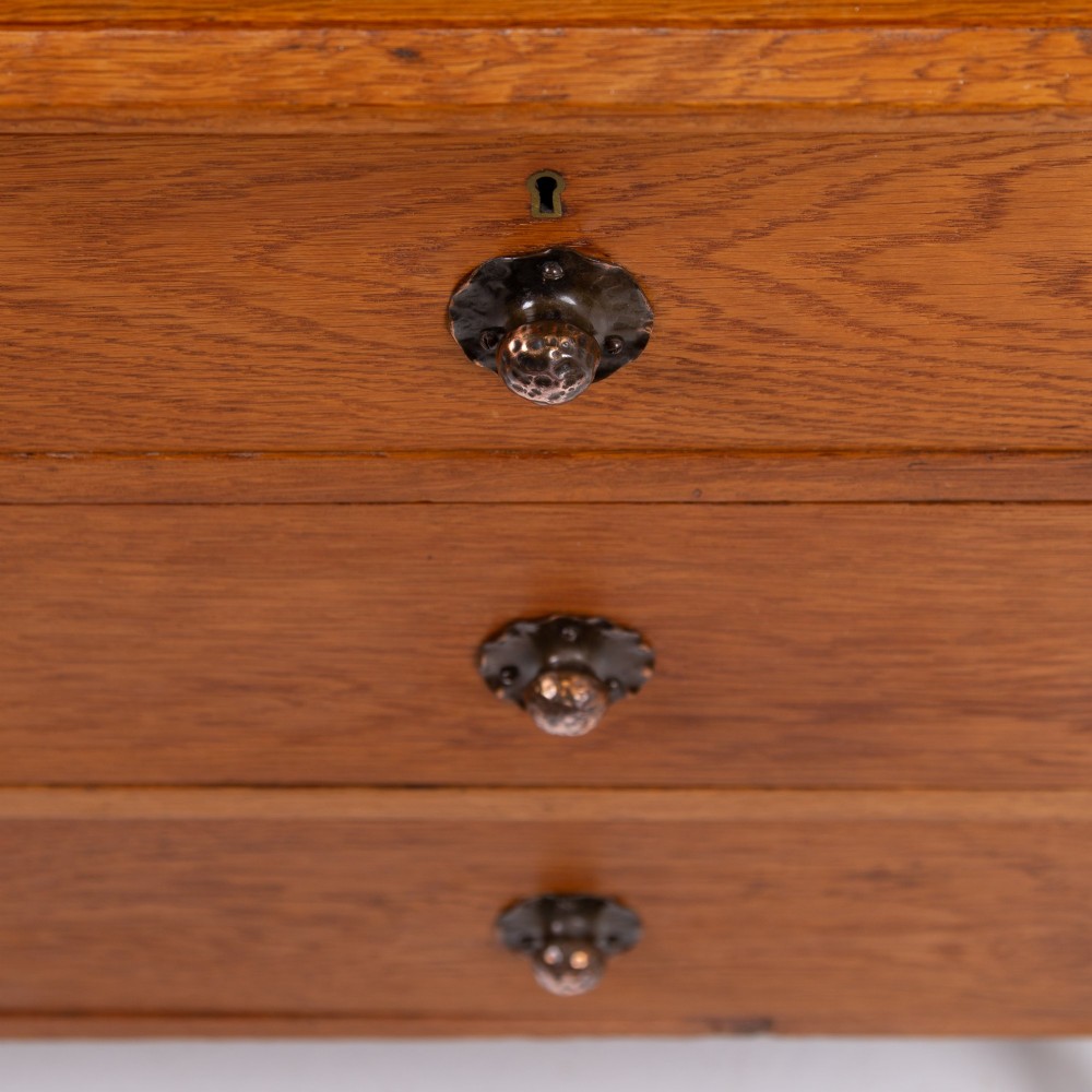 An Arts and Crafts oak dressing chest featuring a superstructure with a central mirror, inlaid side panels, and small jewellery drawers above a chest of drawers. View VI
