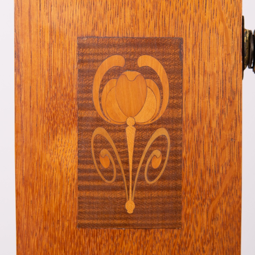 An Arts and Crafts oak dressing chest featuring a superstructure with a central mirror, inlaid side panels, and small jewellery drawers above a chest of drawers. View VII
