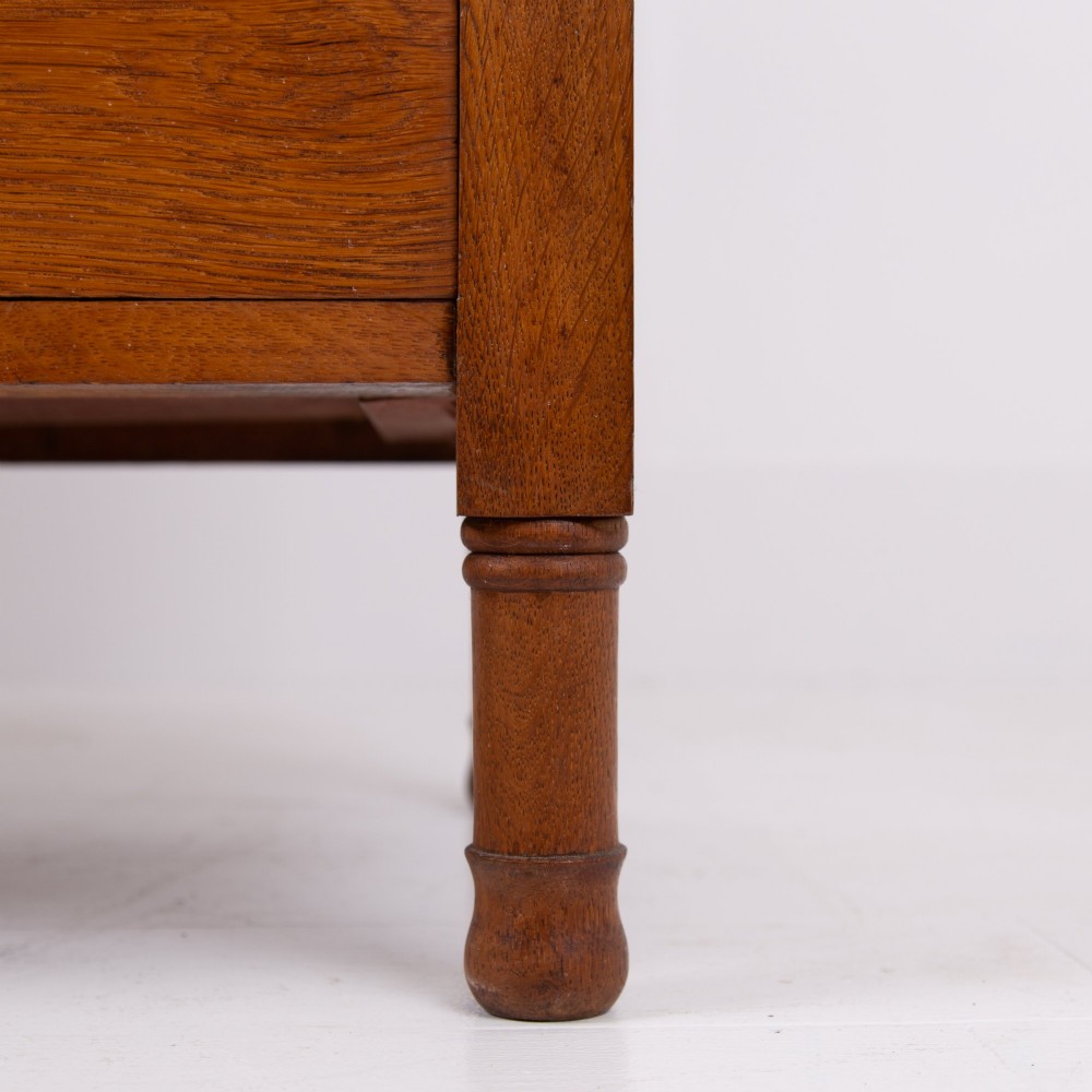 An Arts and Crafts oak dressing chest featuring a superstructure with a central mirror, inlaid side panels, and small jewellery drawers above a chest of drawers. View IX