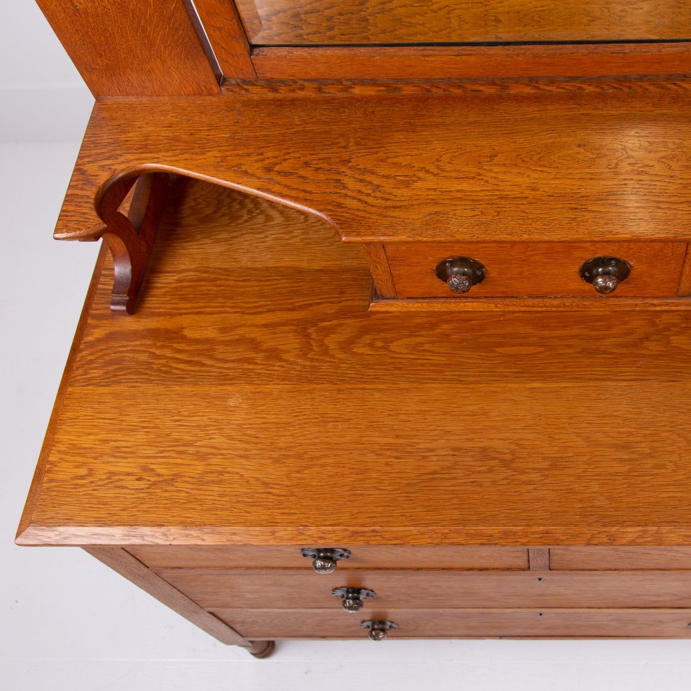 An Arts and Crafts oak dressing chest featuring a superstructure with a central mirror, inlaid side panels, and small jewellery drawers above a chest of drawers. View XIII