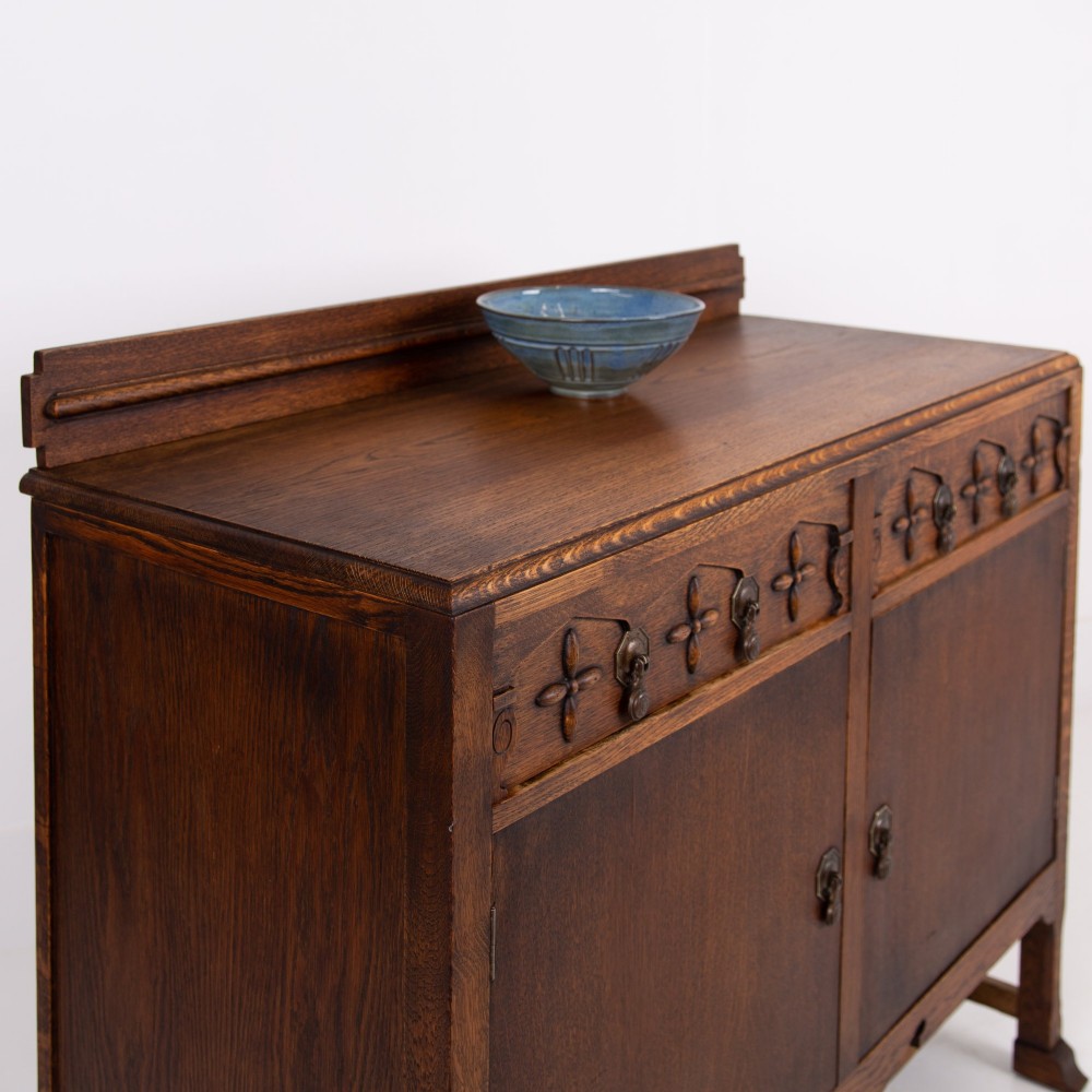 A 1930s warm brown oak sideboard featuring two carved top drawers above a double-door cupboard, supported by block legs and a low stretcher base. View II