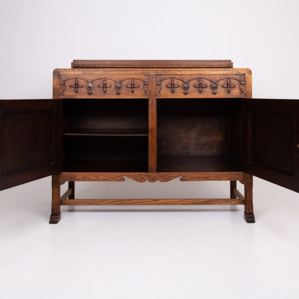A 1930s warm brown oak sideboard featuring two carved top drawers above a double-door cupboard, supported by block legs and a low stretcher base. View VIII
