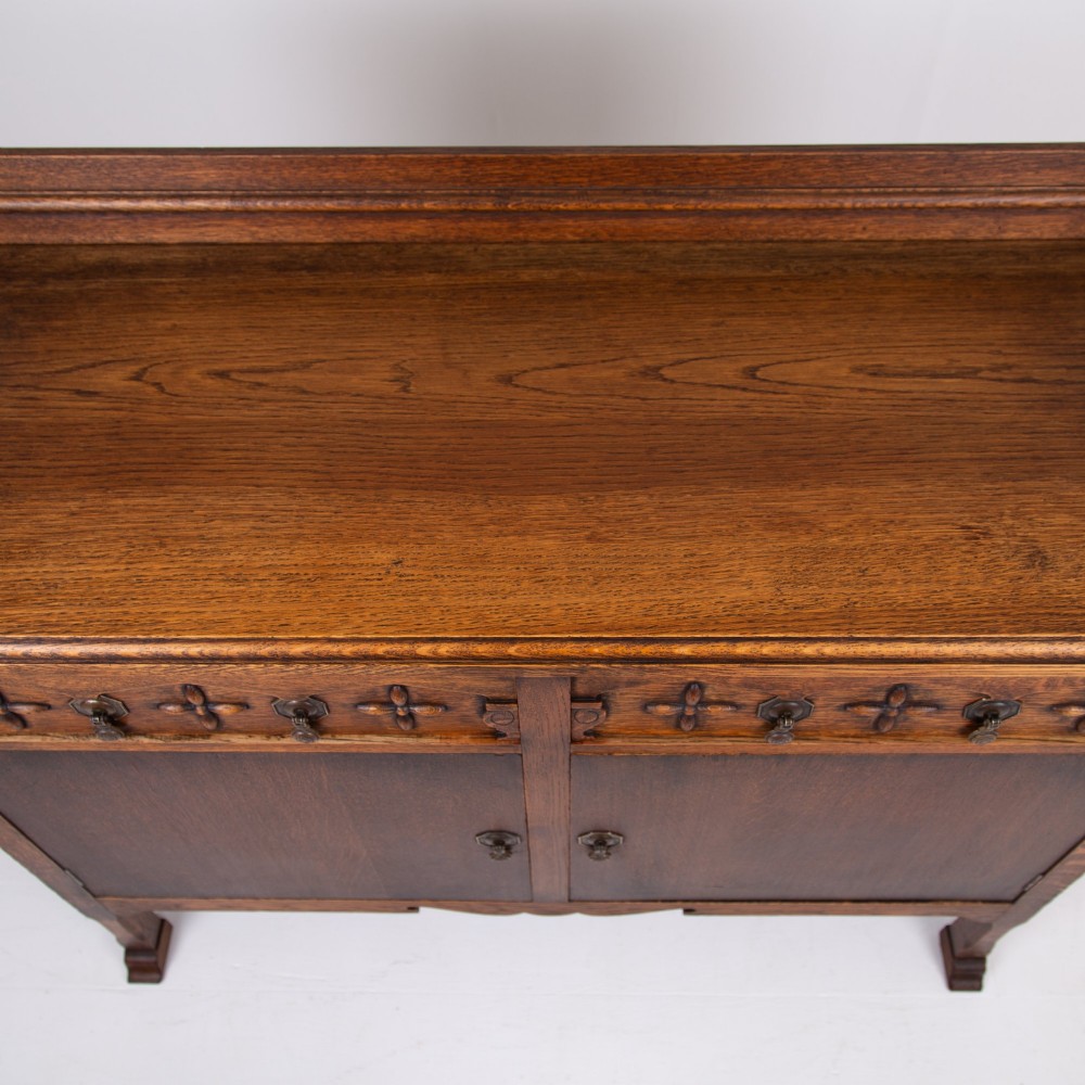 A 1930s warm brown oak sideboard featuring two carved top drawers above a double-door cupboard, supported by block legs and a low stretcher base. View IX