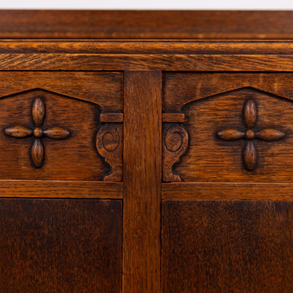 A 1930s warm brown oak sideboard featuring two carved top drawers above a double-door cupboard, supported by block legs and a low stretcher base. View XI