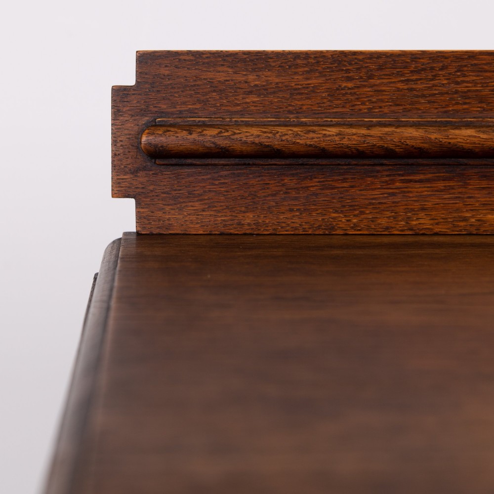 A 1930s warm brown oak sideboard featuring two carved top drawers above a double-door cupboard, supported by block legs and a low stretcher base. View XII