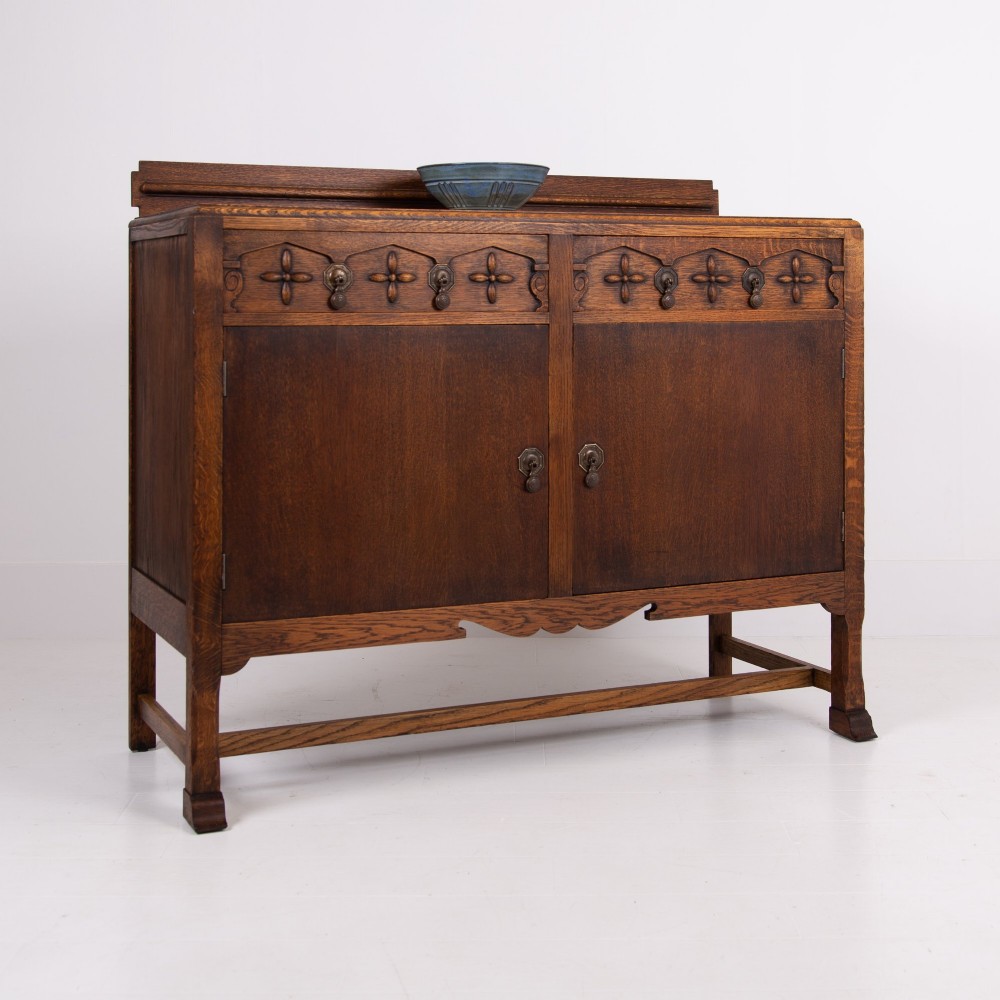 A 1930s warm brown oak sideboard featuring two carved top drawers above a double-door cupboard, supported by block legs and a low stretcher base. View XIV