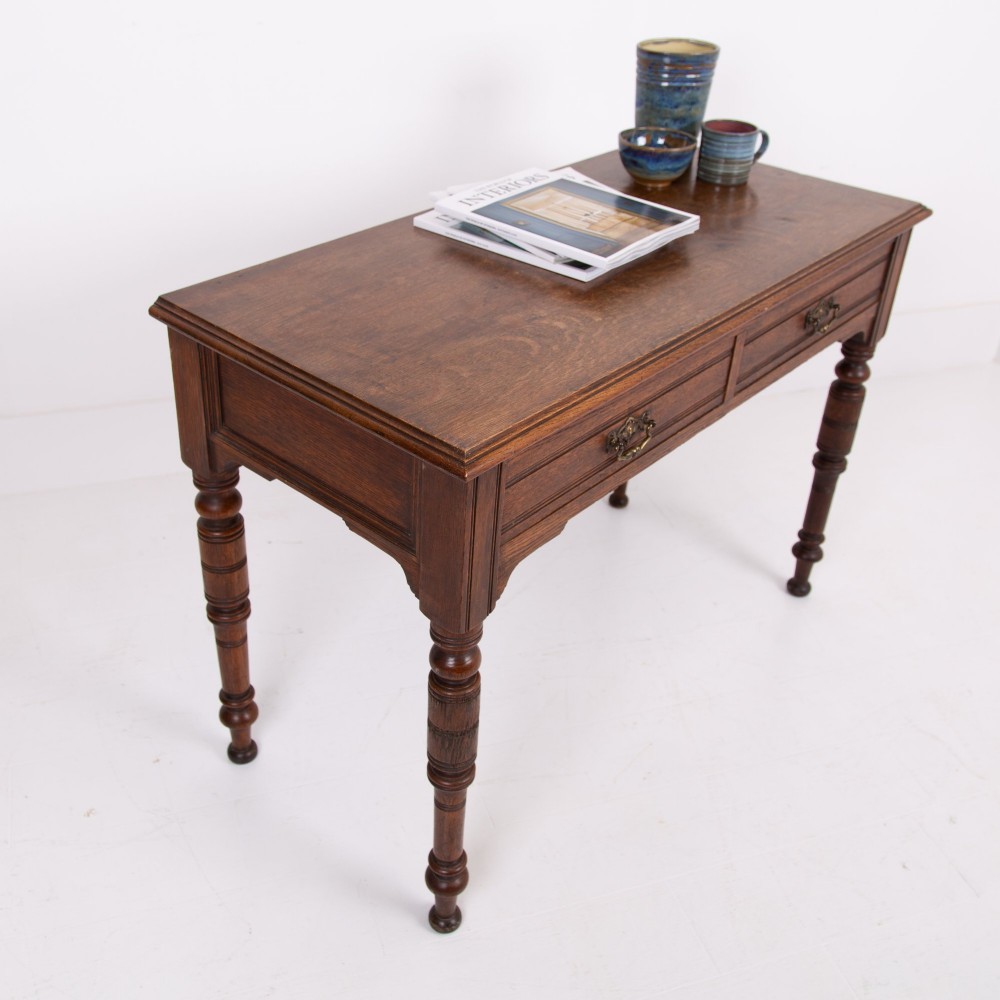A Victorian solid oak writing desk featuring two drawers with brass drop handles and supported by four turned legs. View II