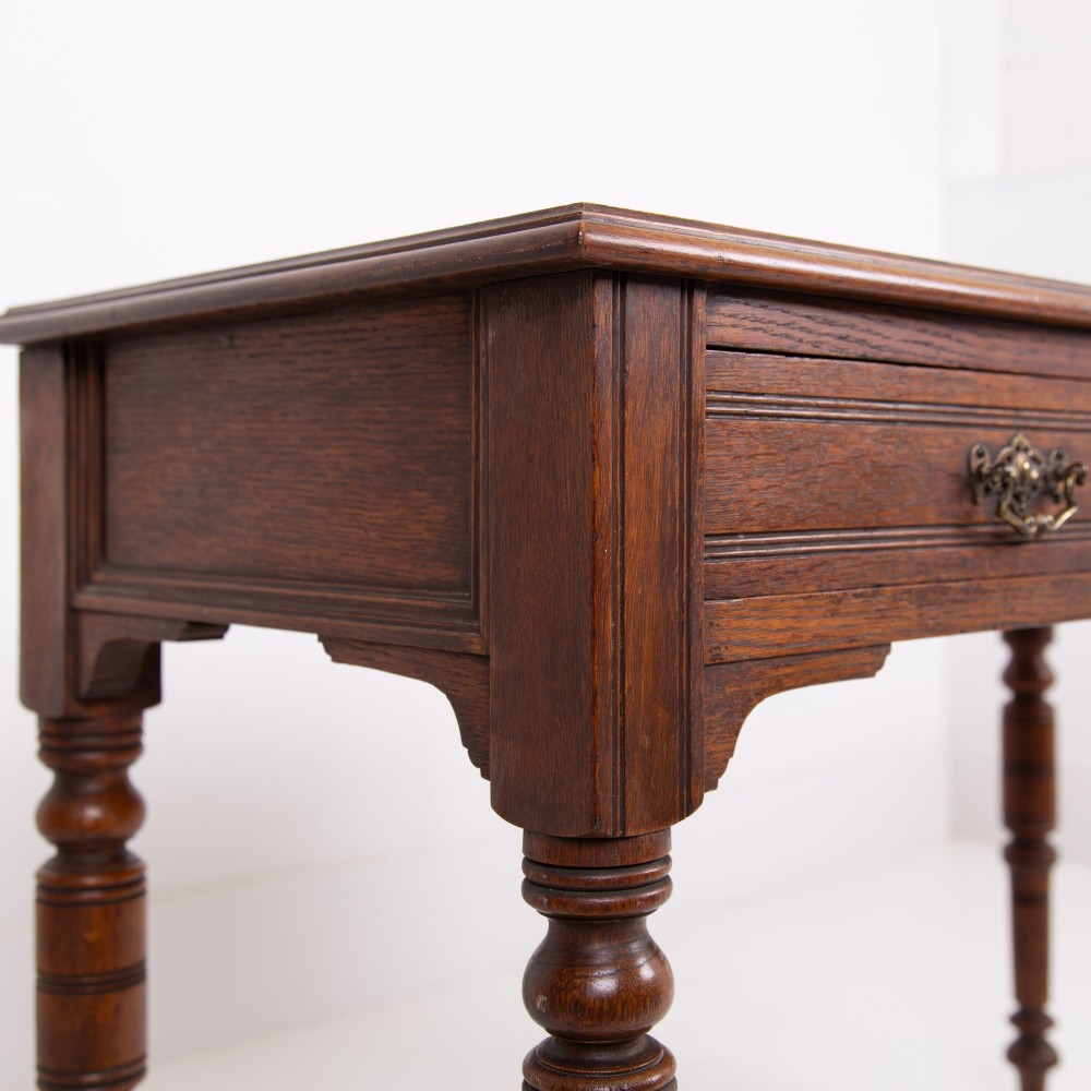 A Victorian solid oak writing desk featuring two drawers with brass drop handles and supported by four turned legs. View V