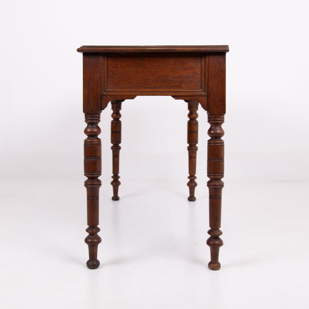 A Victorian solid oak writing desk featuring two drawers with brass drop handles and supported by four turned legs. View VIII