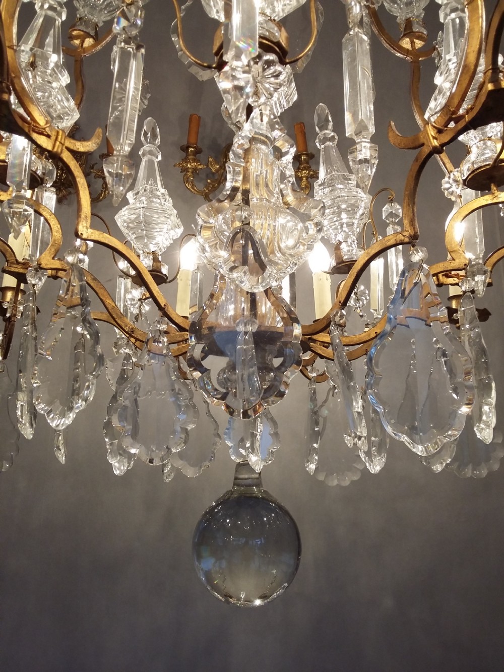 A Louis XV style multi-tiered chandelier featuring curved gilt metal arms, candle sleeves, central glass spires, and faceted crystal drops. View VII
