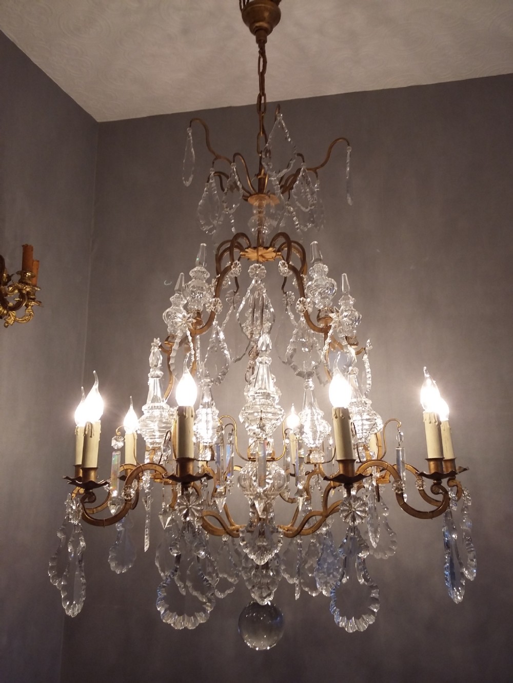 A Louis XV style multi-tiered chandelier featuring curved gilt metal arms, candle sleeves, central glass spires, and faceted crystal drops. View VIII