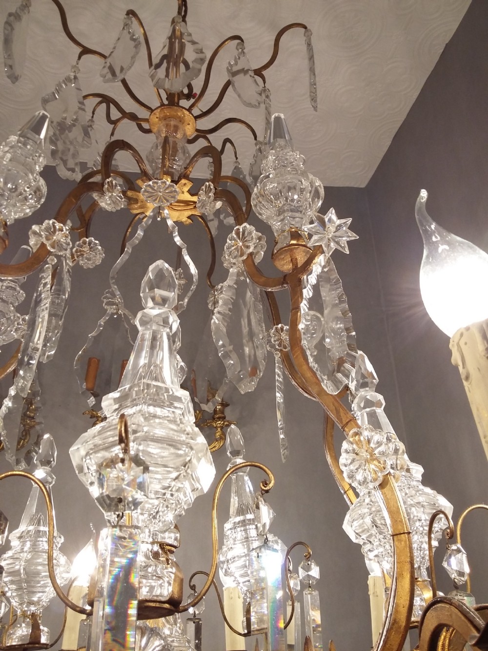 A Louis XV style multi-tiered chandelier featuring curved gilt metal arms, candle sleeves, central glass spires, and faceted crystal drops. View IX