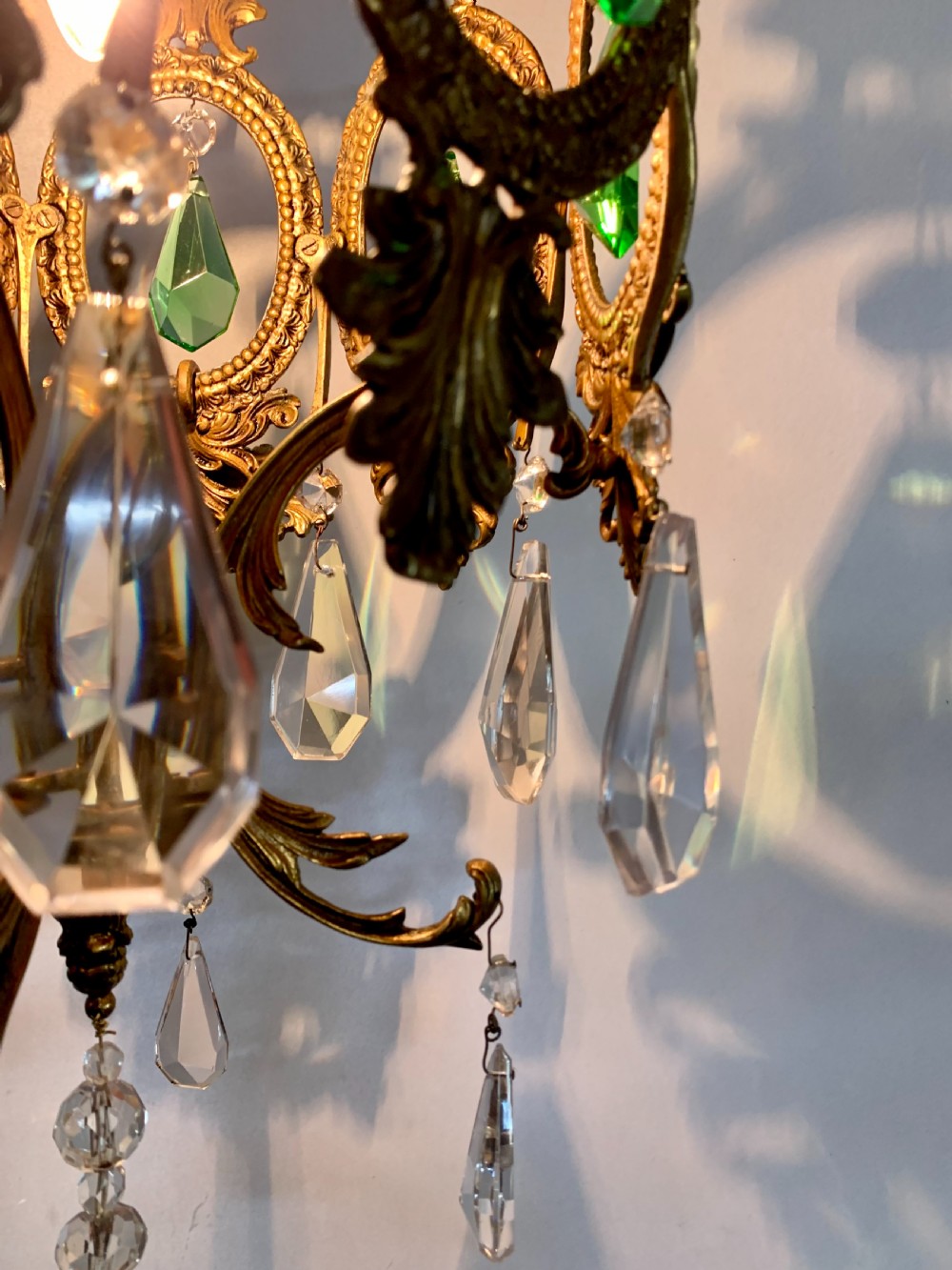 An ornate gilded bronze Florentine pendant light featuring scrolling leaf motifs, oval frame inserts enclosing faceted green crystals, and hanging clear glass prisms. View IV