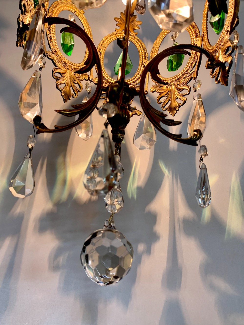 An ornate gilded bronze Florentine pendant light featuring scrolling leaf motifs, oval frame inserts enclosing faceted green crystals, and hanging clear glass prisms. View V