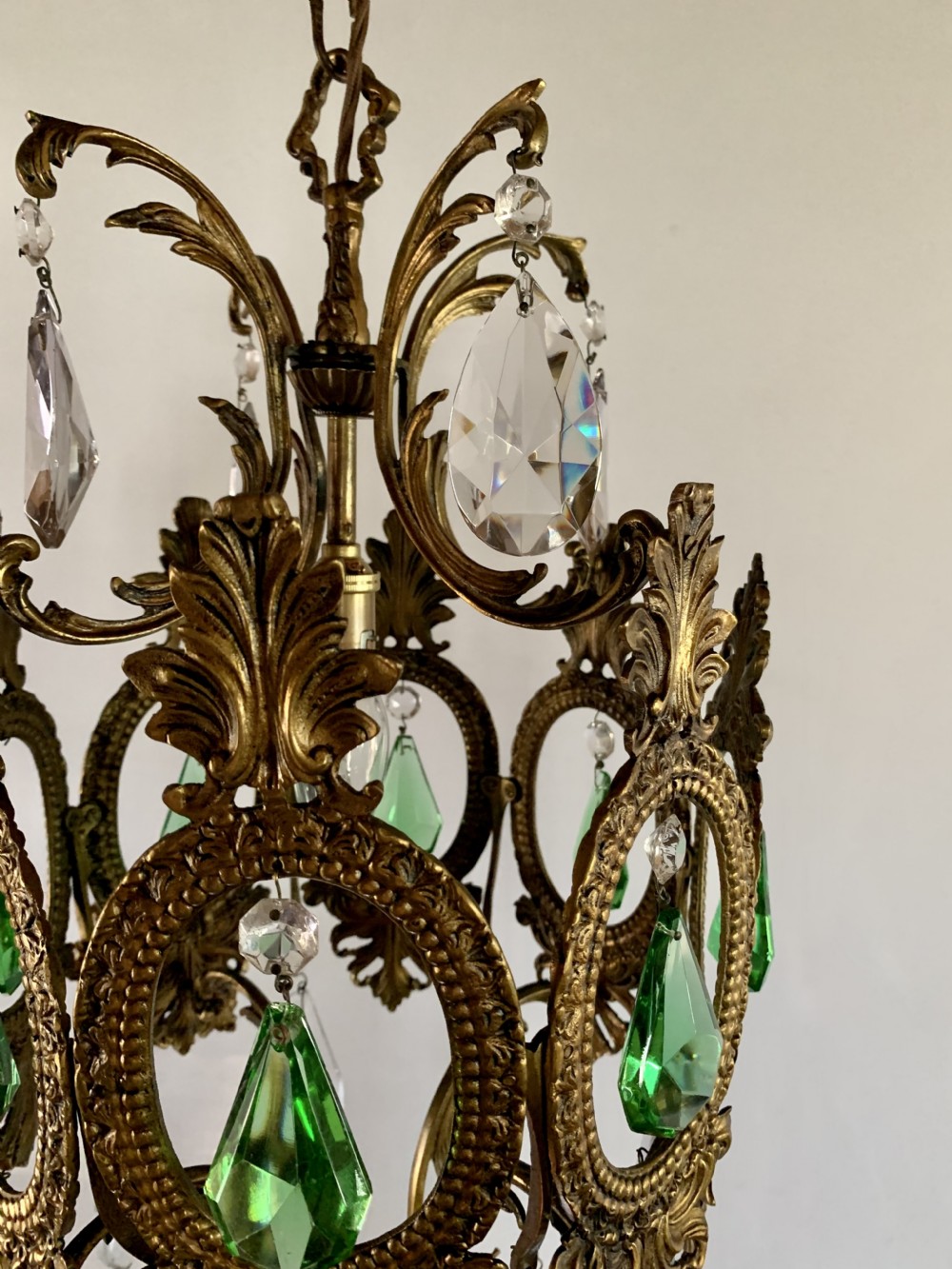 An ornate gilded bronze Florentine pendant light featuring scrolling leaf motifs, oval frame inserts enclosing faceted green crystals, and hanging clear glass prisms. View VII