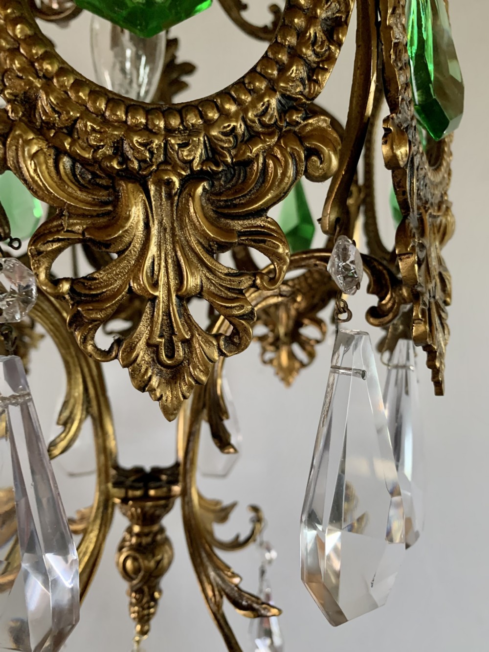An ornate gilded bronze Florentine pendant light featuring scrolling leaf motifs, oval frame inserts enclosing faceted green crystals, and hanging clear glass prisms. View IX
