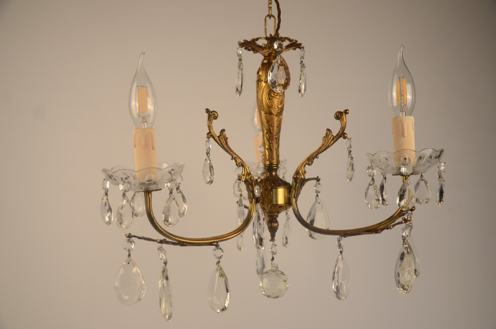 A three-arm gilt brass Italian chandelier decorated with hanging glass teardrop prisms and candle-effect light fittings.