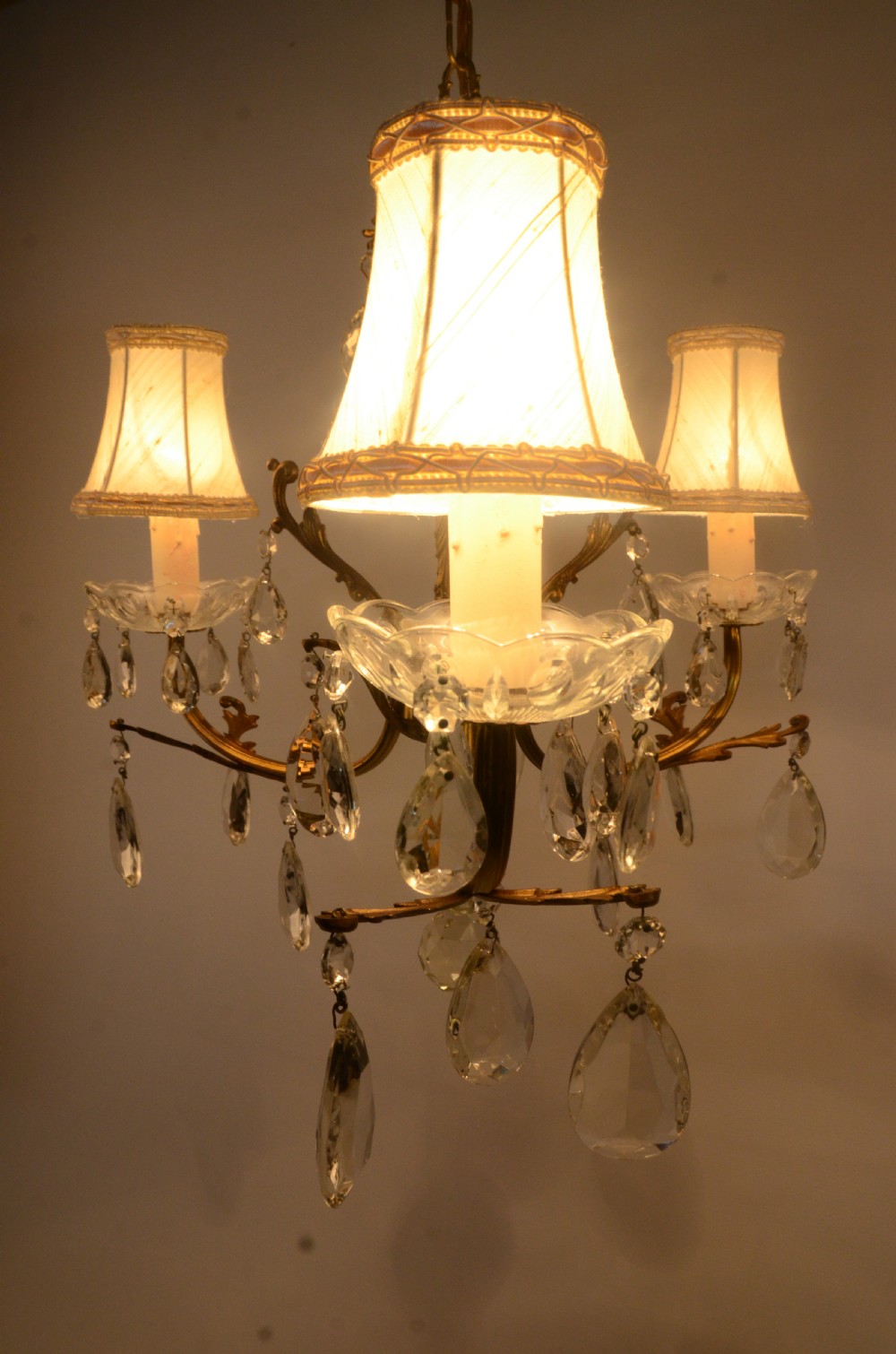 A three-arm gilt brass Italian chandelier decorated with hanging glass teardrop prisms and candle-effect light fittings. View II