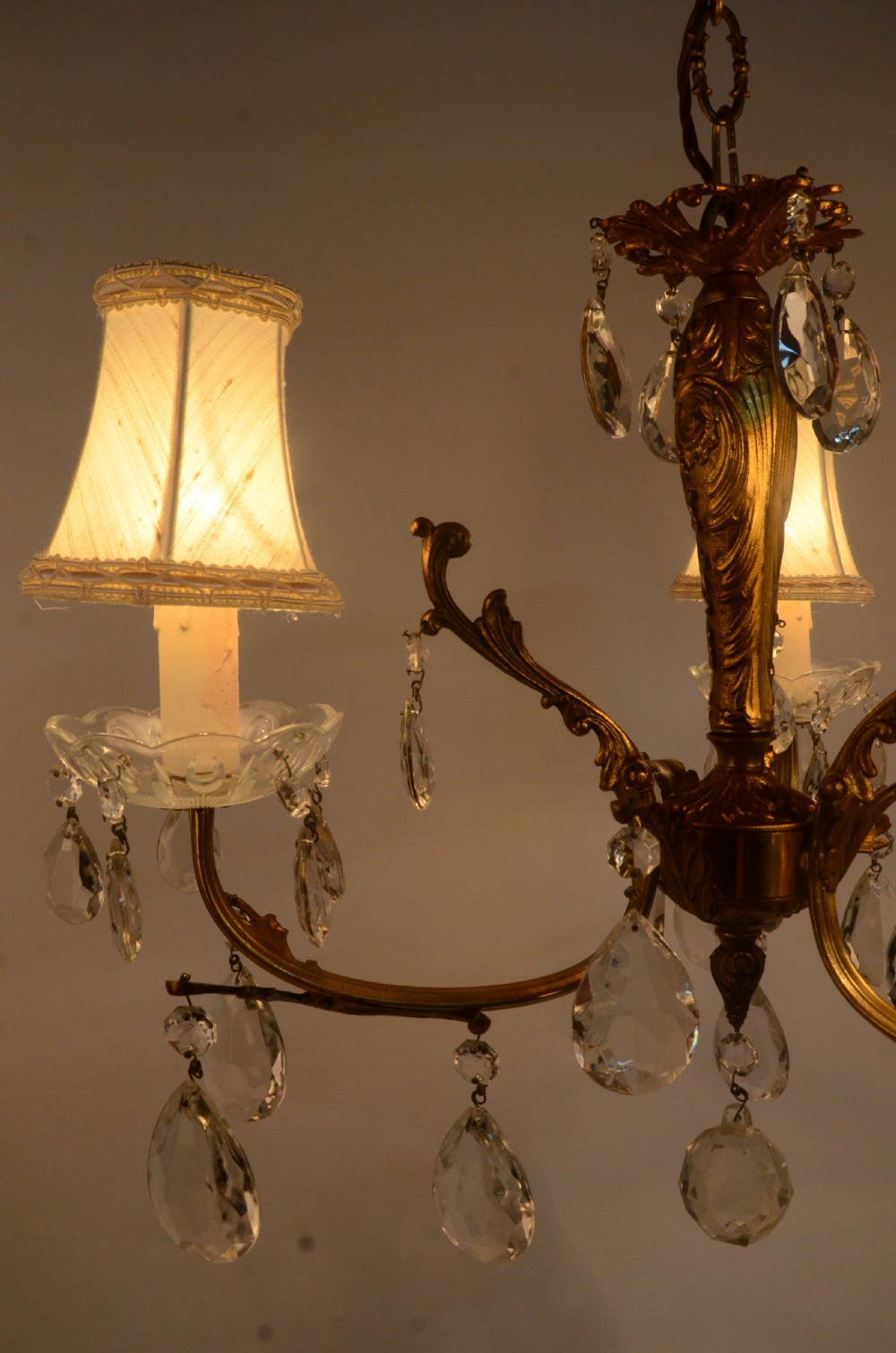 A three-arm gilt brass Italian chandelier decorated with hanging glass teardrop prisms and candle-effect light fittings. View III