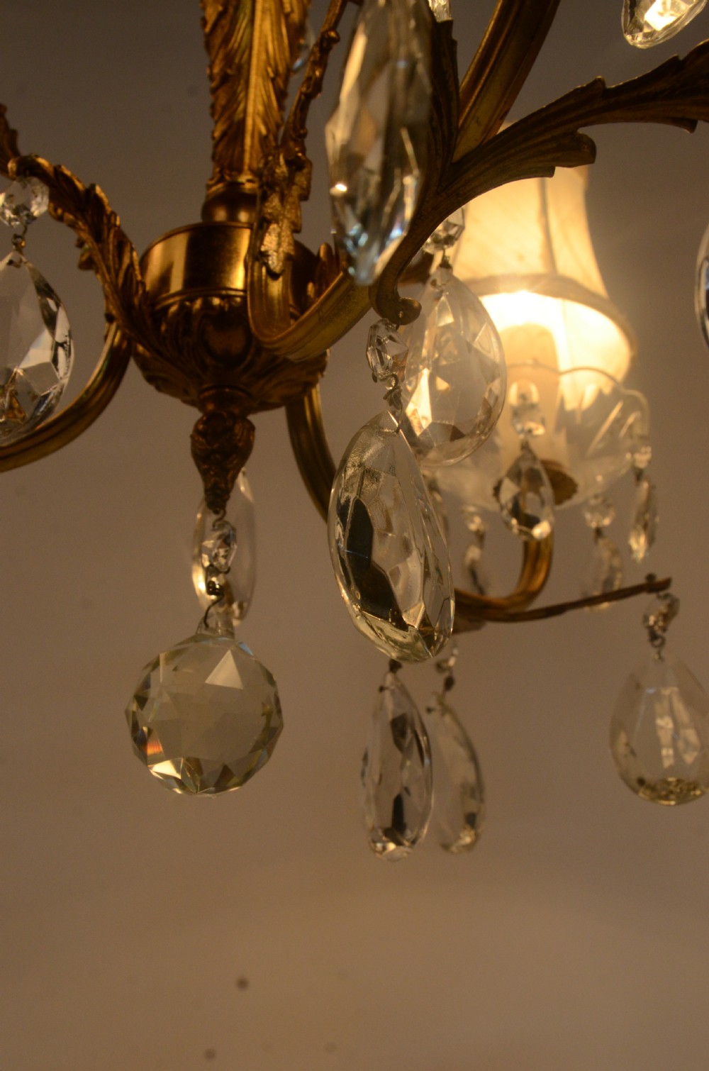A three-arm gilt brass Italian chandelier decorated with hanging glass teardrop prisms and candle-effect light fittings. View IV