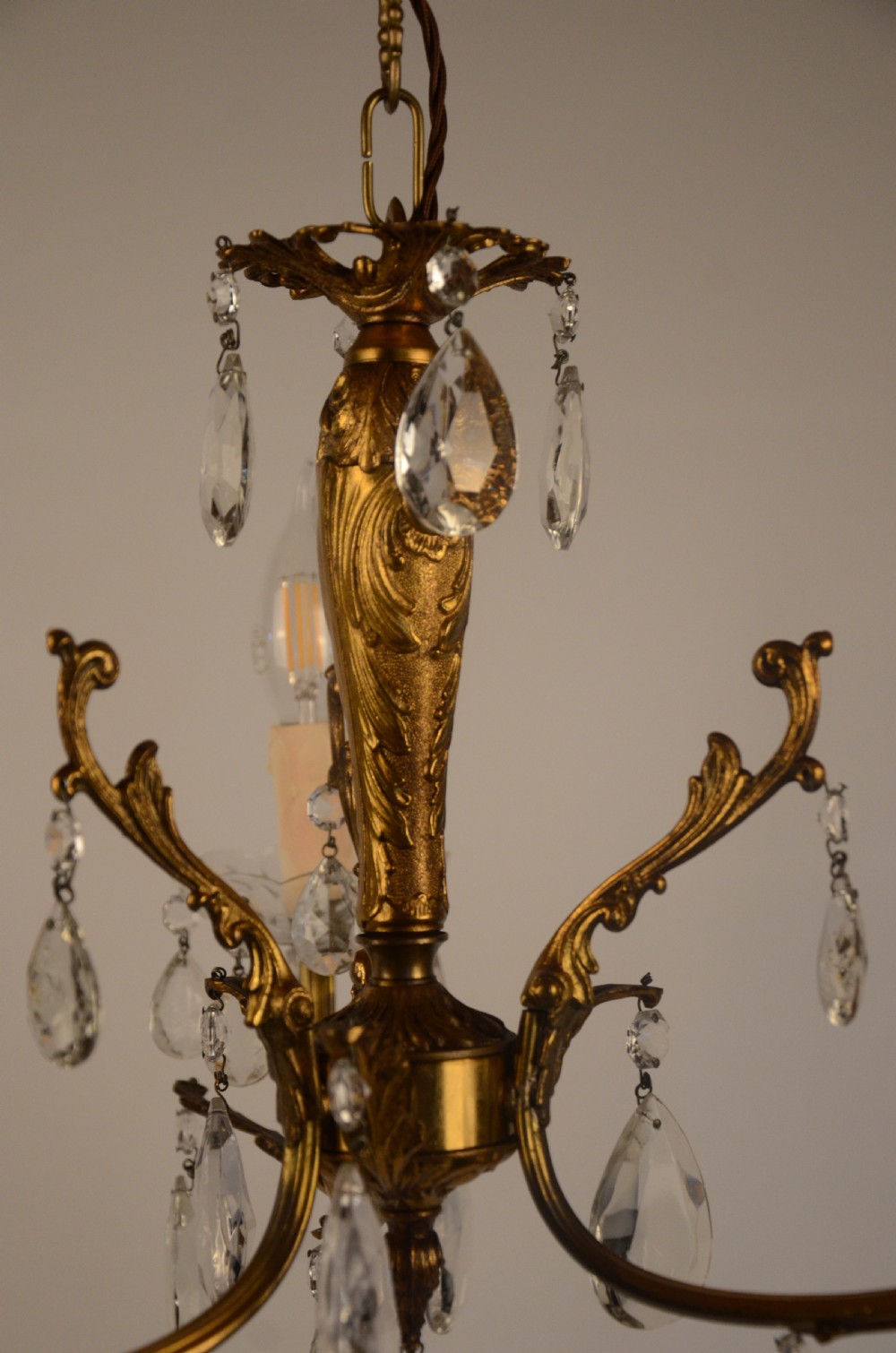 A three-arm gilt brass Italian chandelier decorated with hanging glass teardrop prisms and candle-effect light fittings. View V