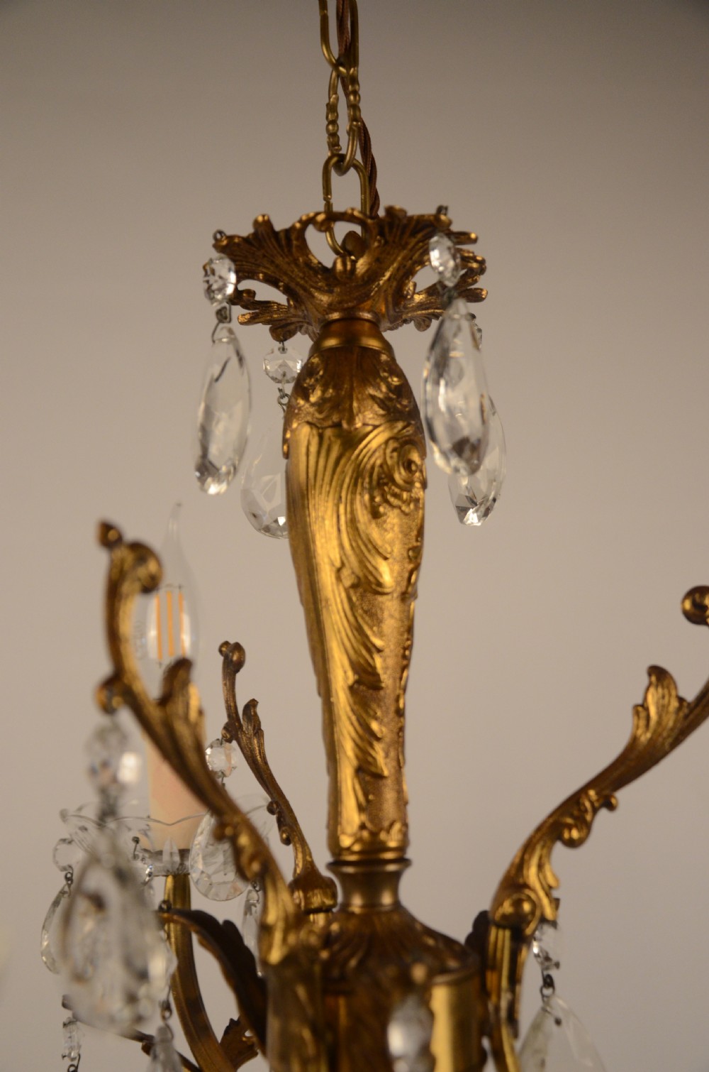 A three-arm gilt brass Italian chandelier decorated with hanging glass teardrop prisms and candle-effect light fittings. View VI