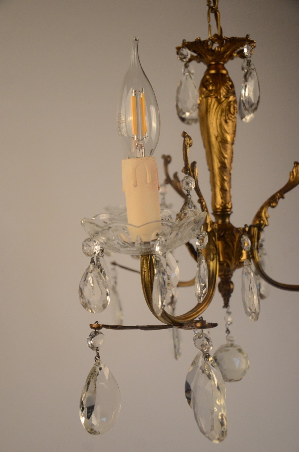 A three-arm gilt brass Italian chandelier decorated with hanging glass teardrop prisms and candle-effect light fittings. View VII