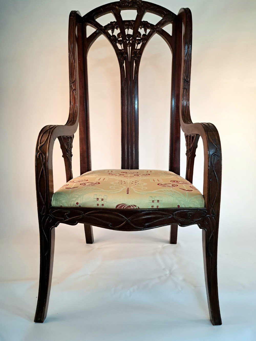An Art Nouveau carved dark wood armchair featuring organic plant-inspired carved backrest detailing and a light green upholstered seat.