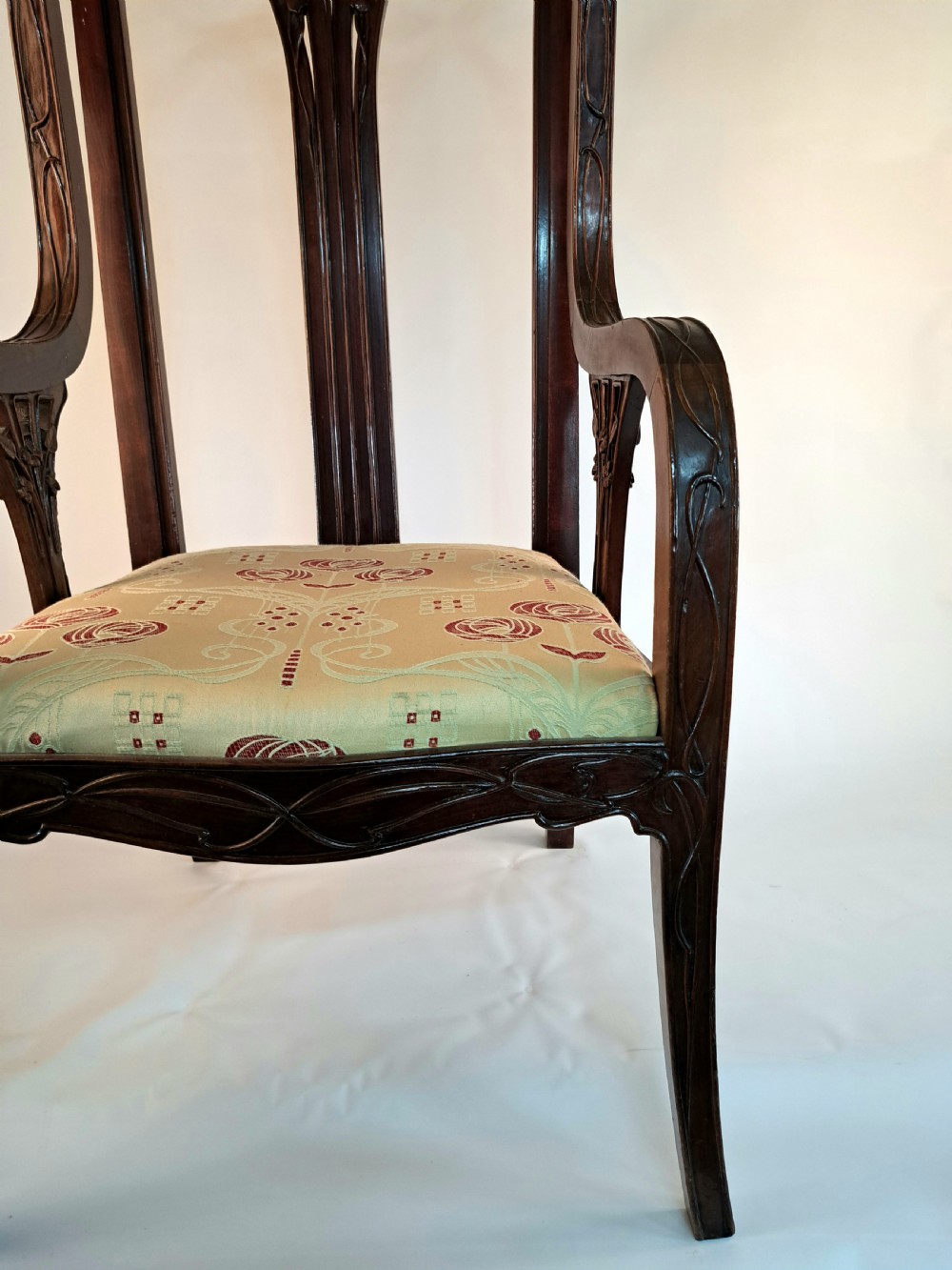 An Art Nouveau carved dark wood armchair featuring organic plant-inspired carved backrest detailing and a light green upholstered seat. View II