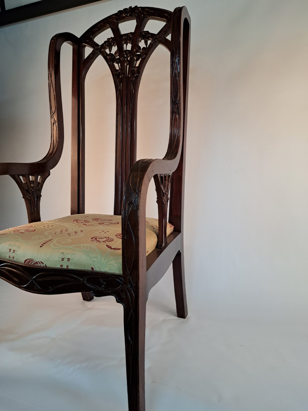 An Art Nouveau carved dark wood armchair featuring organic plant-inspired carved backrest detailing and a light green upholstered seat. View III