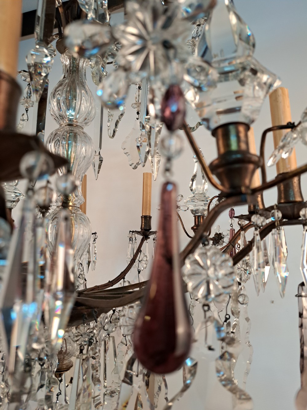 A multi-arm French crystal chandelier with candle-style light sockets, clear faceted glass prisms, and purple teardrop pendants on a dark wrought iron frame. View VII