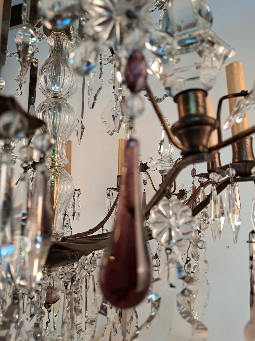 A multi-arm French crystal chandelier with candle-style light sockets, clear faceted glass prisms, and purple teardrop pendants on a dark wrought iron frame. View VIII