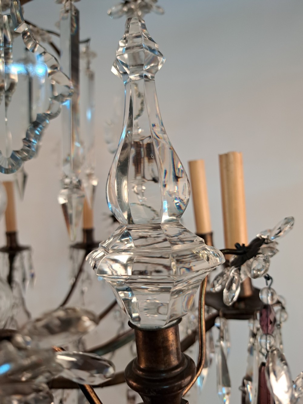 A multi-arm French crystal chandelier with candle-style light sockets, clear faceted glass prisms, and purple teardrop pendants on a dark wrought iron frame. View IX