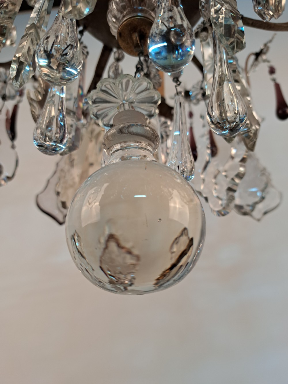 A multi-arm French crystal chandelier with candle-style light sockets, clear faceted glass prisms, and purple teardrop pendants on a dark wrought iron frame. View X
