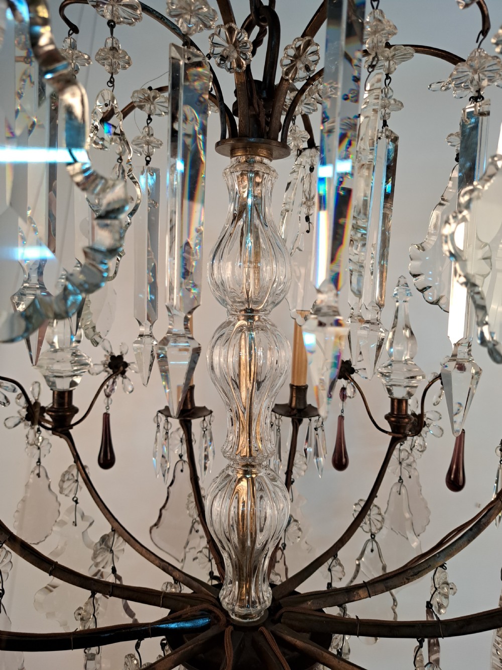 A multi-arm French crystal chandelier with candle-style light sockets, clear faceted glass prisms, and purple teardrop pendants on a dark wrought iron frame. View XVIII