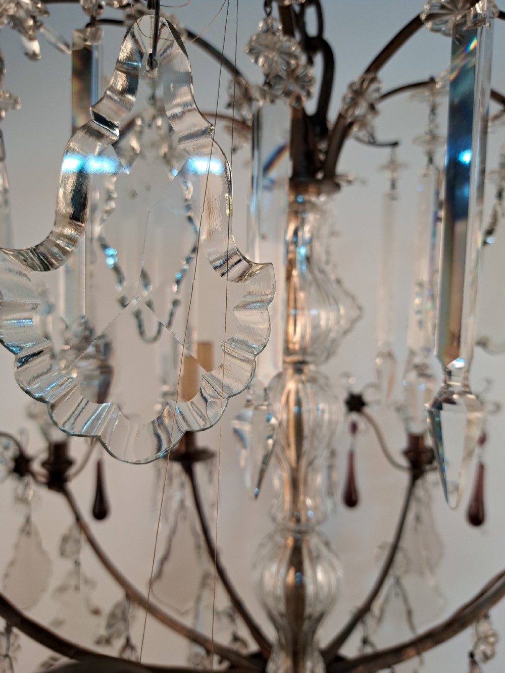 A multi-arm French crystal chandelier with candle-style light sockets, clear faceted glass prisms, and purple teardrop pendants on a dark wrought iron frame. View XIX