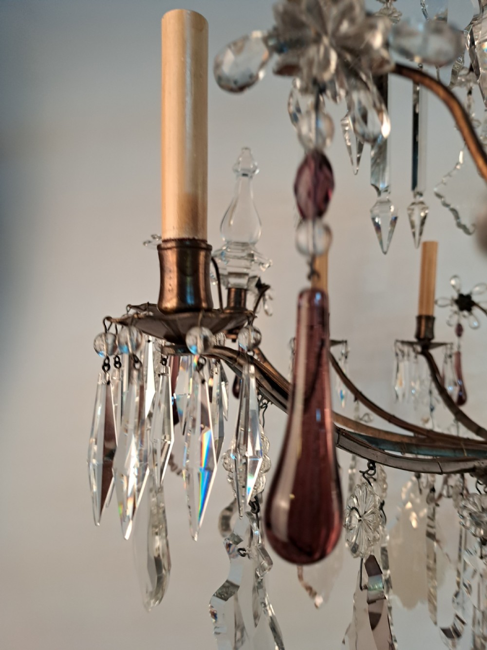 A multi-arm French crystal chandelier with candle-style light sockets, clear faceted glass prisms, and purple teardrop pendants on a dark wrought iron frame. View XXV