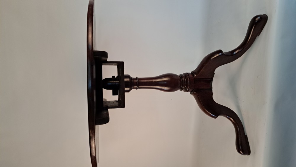 A Georgian mahogany tilt-top table with a circular timber top tilted vertically above a vase-turned pedestal stem and three cabriole legs. View VI