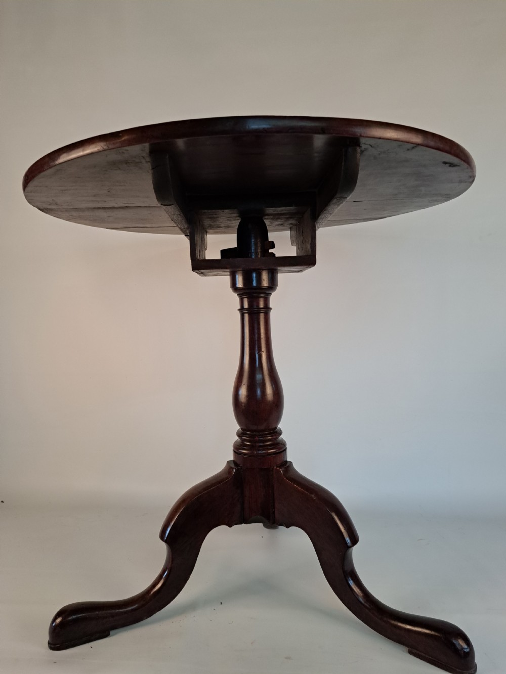 A Georgian mahogany tilt-top table with a circular timber top tilted vertically above a vase-turned pedestal stem and three cabriole legs. View VII