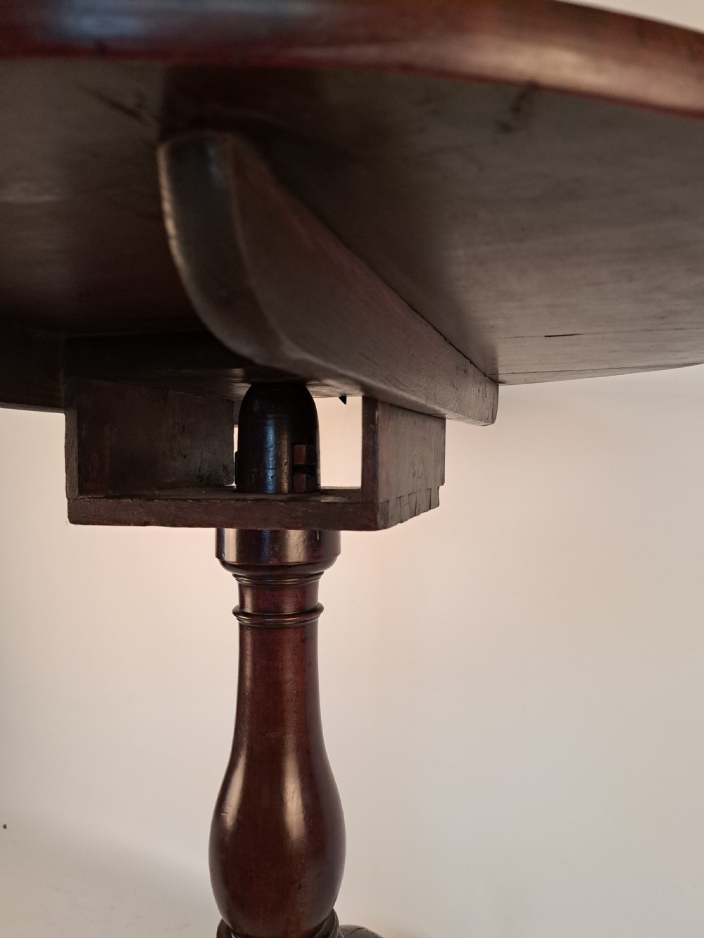 A Georgian mahogany tilt-top table with a circular timber top tilted vertically above a vase-turned pedestal stem and three cabriole legs. View X