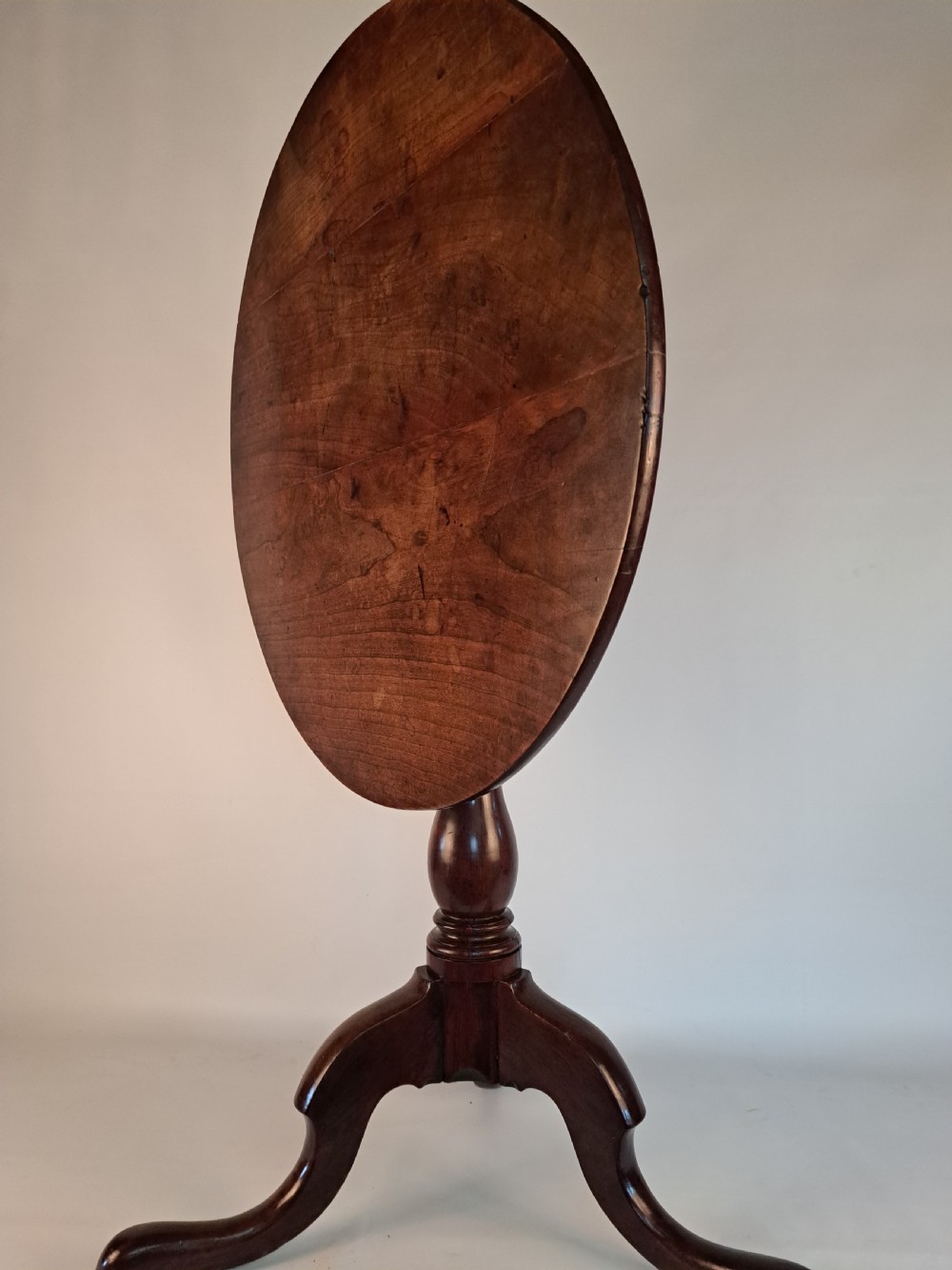 A Georgian mahogany tilt-top table with a circular timber top tilted vertically above a vase-turned pedestal stem and three cabriole legs. View XX