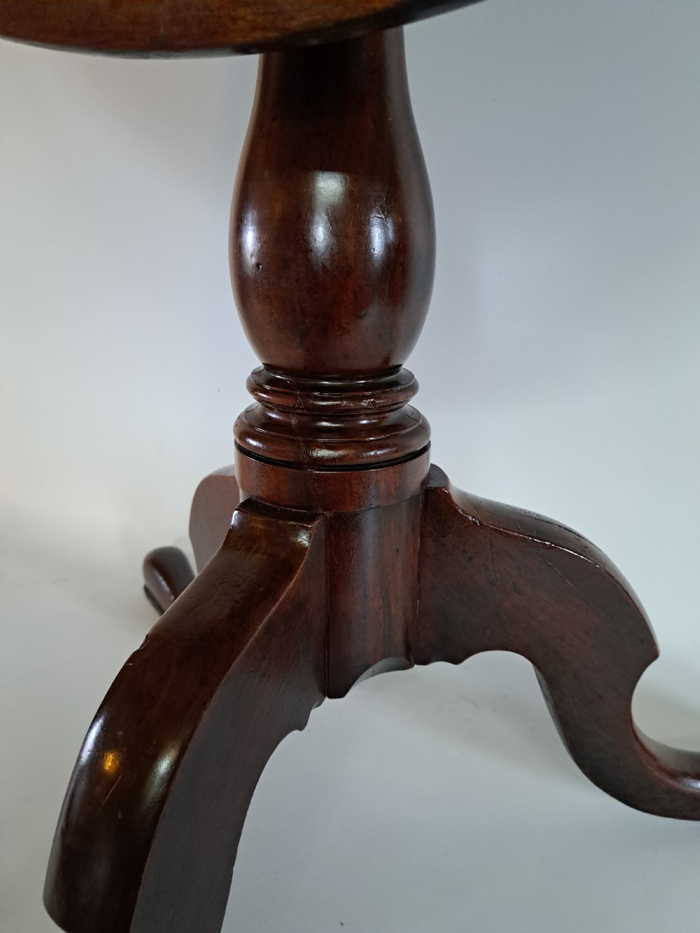 A Georgian mahogany tilt-top table with a circular timber top tilted vertically above a vase-turned pedestal stem and three cabriole legs. View XXVI