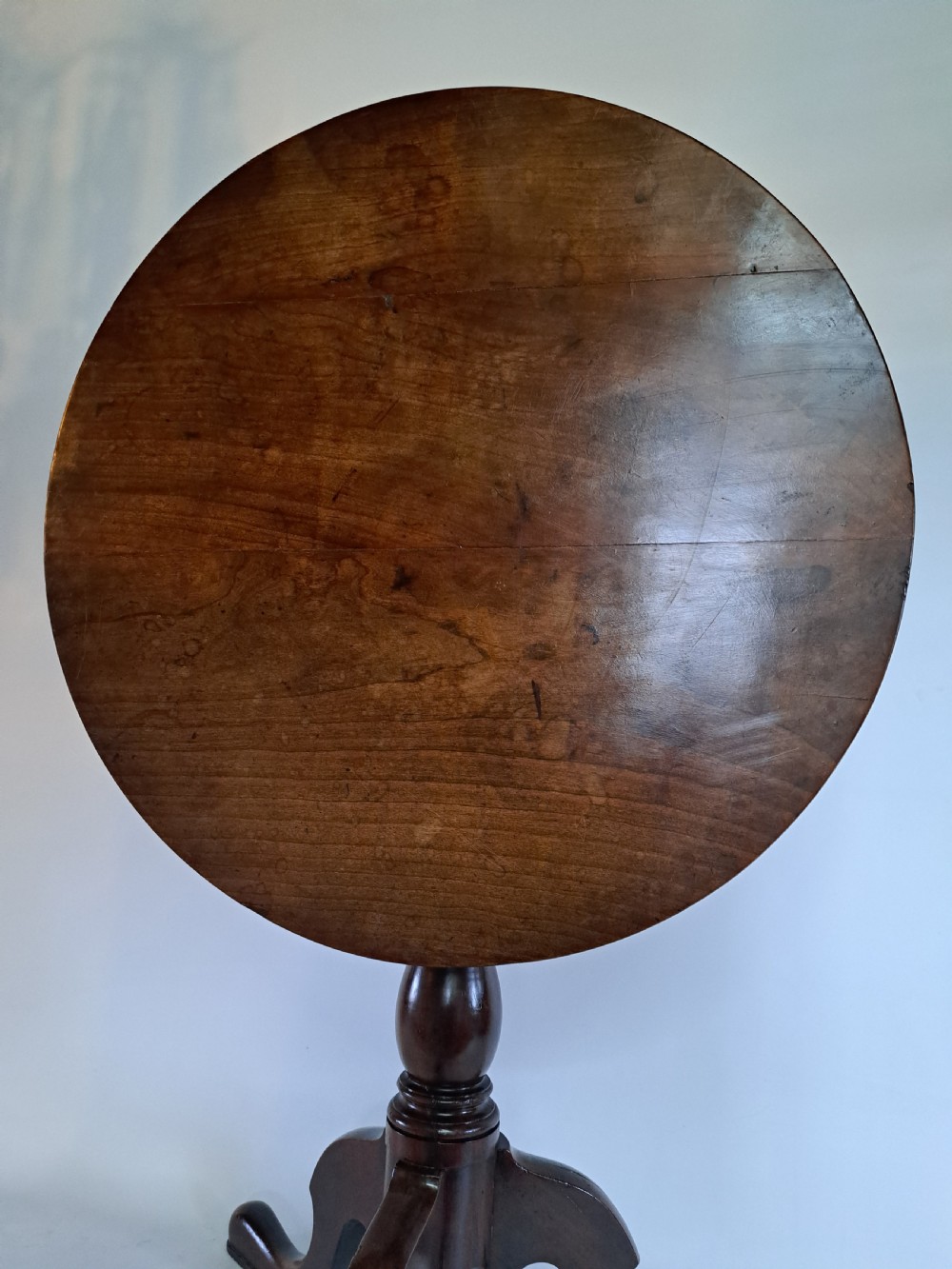 A Georgian mahogany tilt-top table with a circular timber top tilted vertically above a vase-turned pedestal stem and three cabriole legs. View XXVII